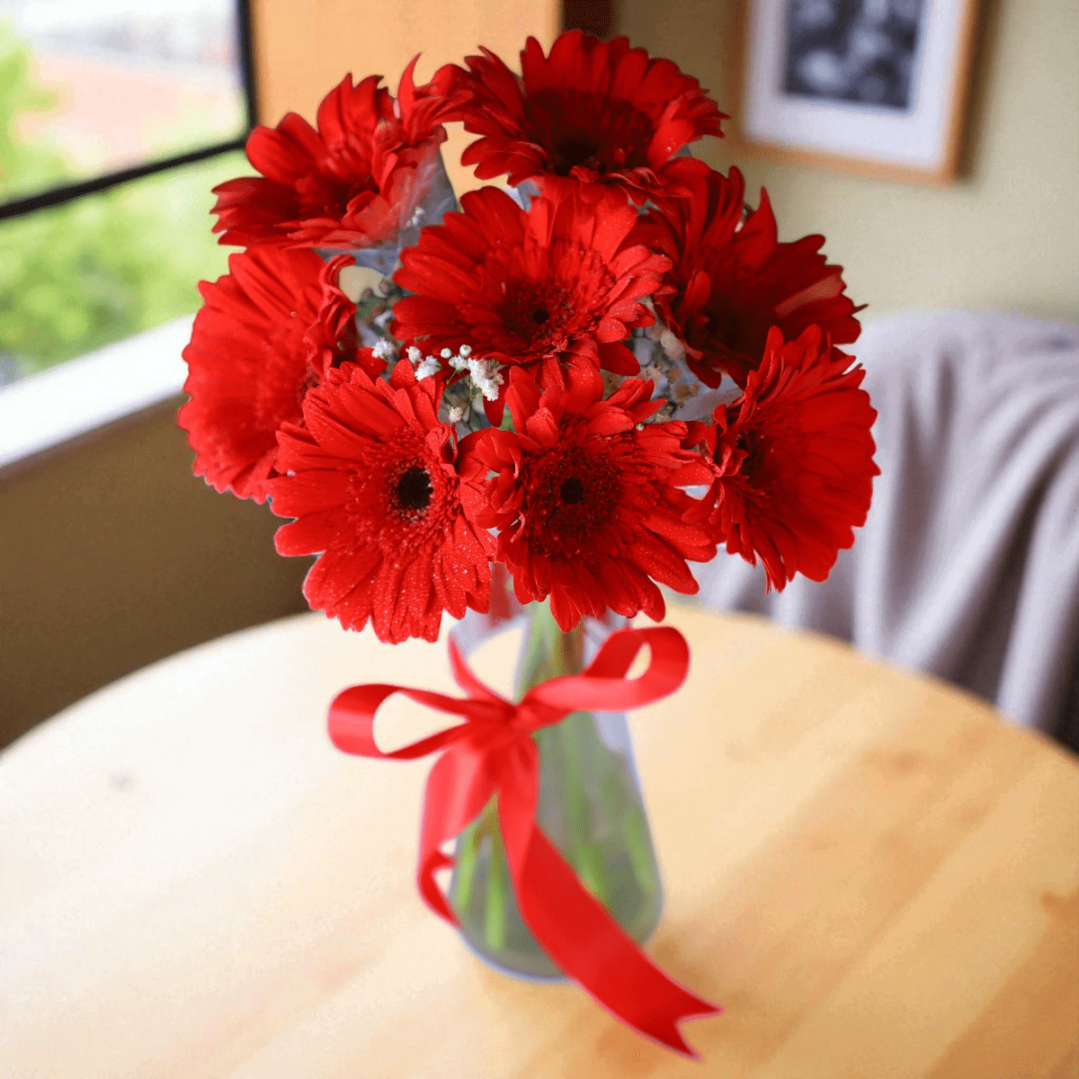 Red gerbera flower bouquet in glass vase with ribbon bow