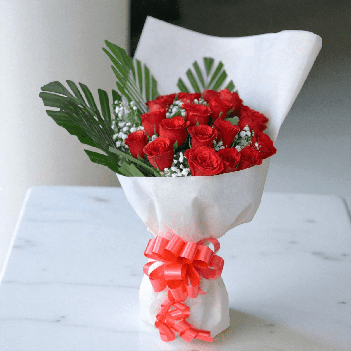 IMG_7708 (2) - Copy Elegant bouquet of red roses in white paper wrap with ribbon, decorated with green foliage.