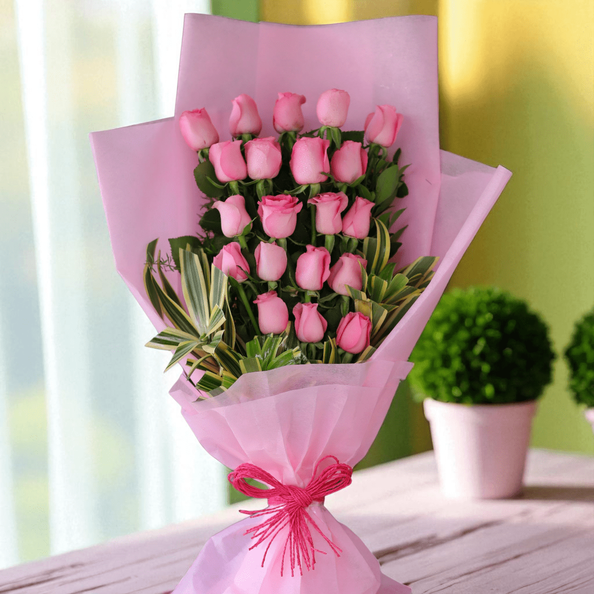 20 pink roses arranged in a one-sided pastel designer wrap with decorative greens.