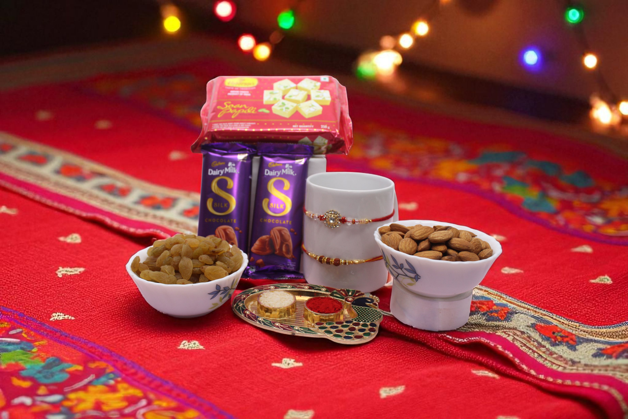 a divine Rudraksh Rakhi and a dazzling Chakri Rakhi, includes 2 Cadbury Dairy Milk Silk bars, a classic 250g Soan Papdi box, premium 100g almonds, and 100g raisins, - YHOJA.COM