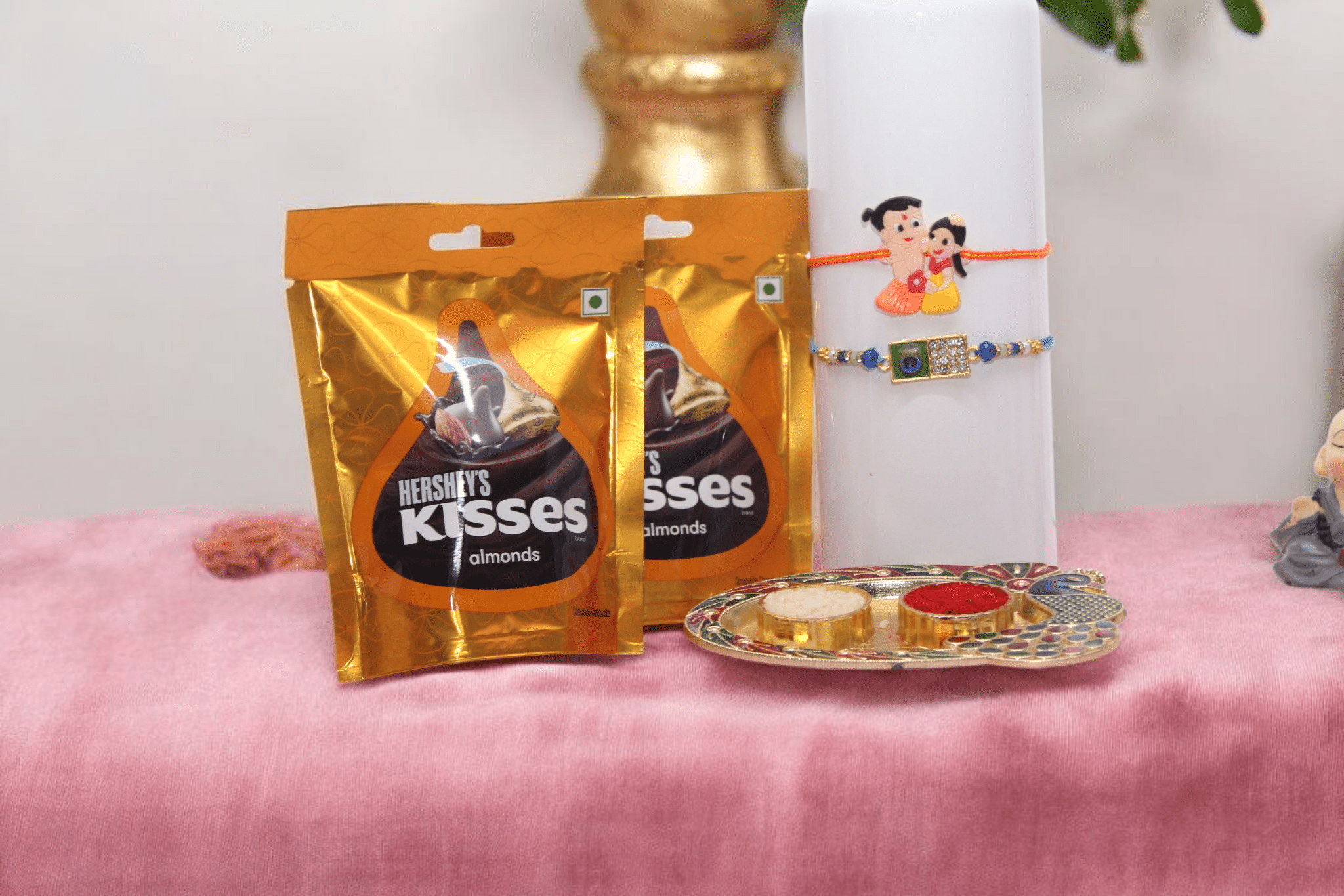 a cute Kid Rakhi, a classy Peacock Stone Rakhi, and two packs of Hershey’s Kisses Almond chocolates. - YHOJA.COM