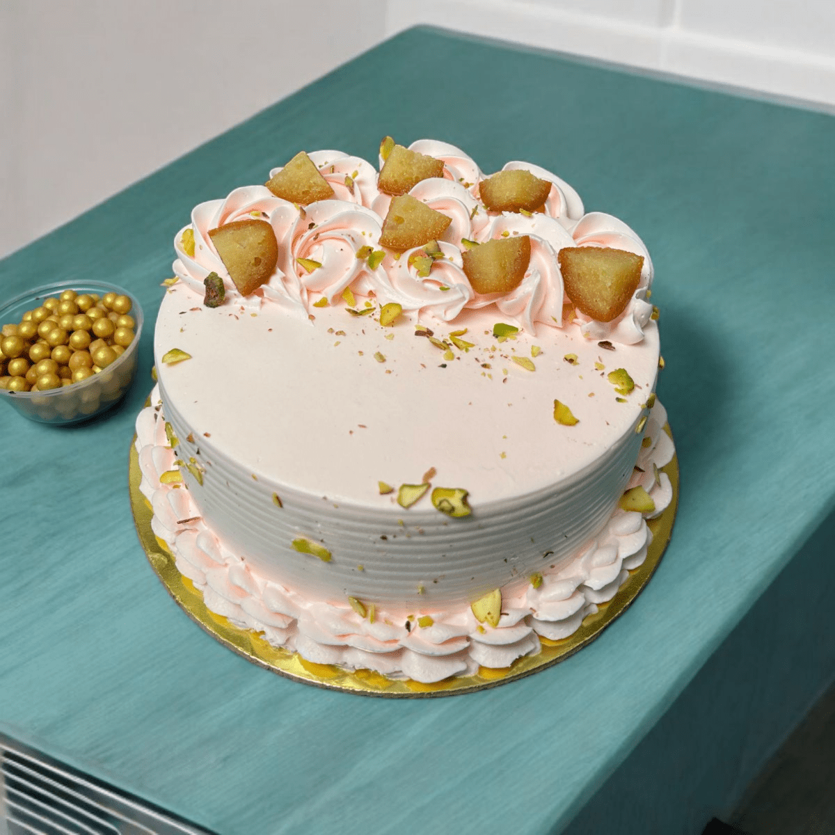 Photoroom-20250227_140522 Gulab Jamun Fusion Cake topped with gulab jamuns, whipped cream rosettes, and pistachio sprinkles on a golden base.